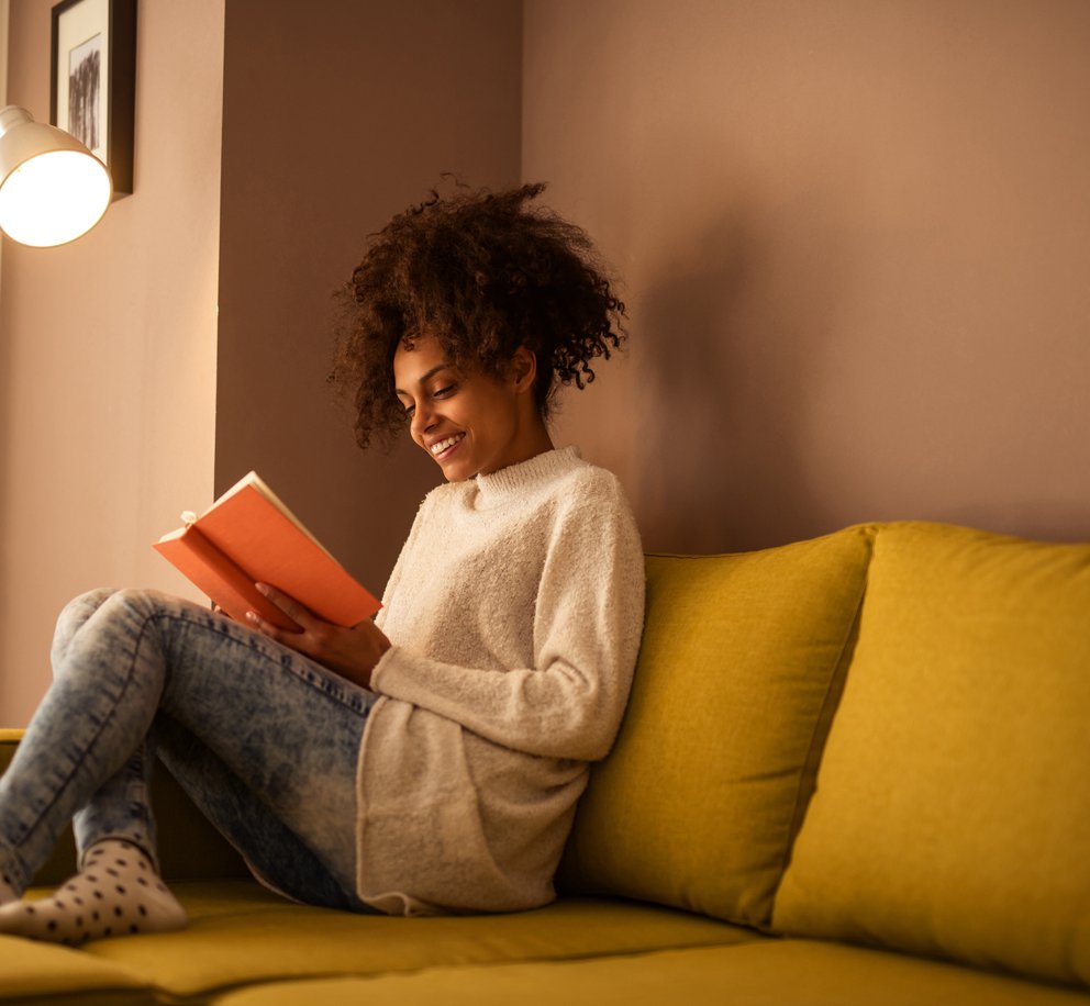Foto van een vrouw die een boek leest op de bank in een heerlijk warm huis.