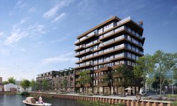 Een gebouw van 9 verdiepingen met lagere gebouwen eraan vast. Op de voorgrond is een kanaal.