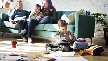 Gezinsleven: moeder met kind op de bank met een zoontje die op de voorgrond op de vloer een tekent