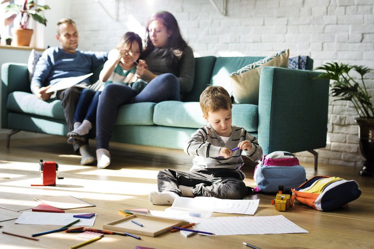 Gezinsleven: moeder met kind op de bank met een zoontje die op de voorgrond op de vloer een tekent