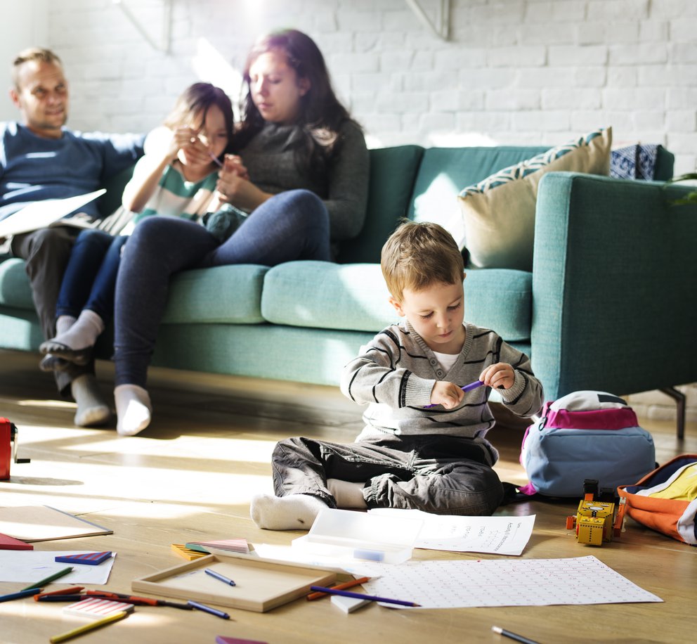 Gezinsleven: moeder met kind op de bank met een zoontje die op de voorgrond op de vloer een tekent