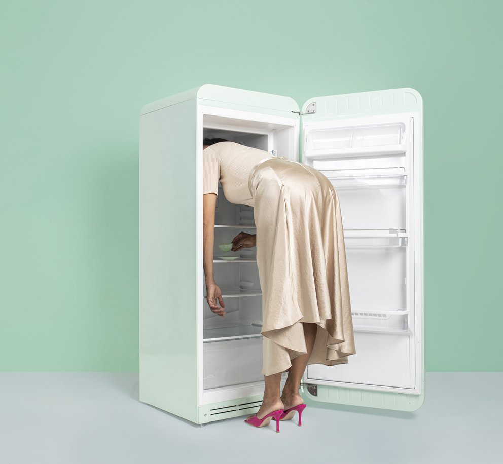 Een vrouw die op zoek is naar verkoeling en haar hoofd in de koelkast laat rusten