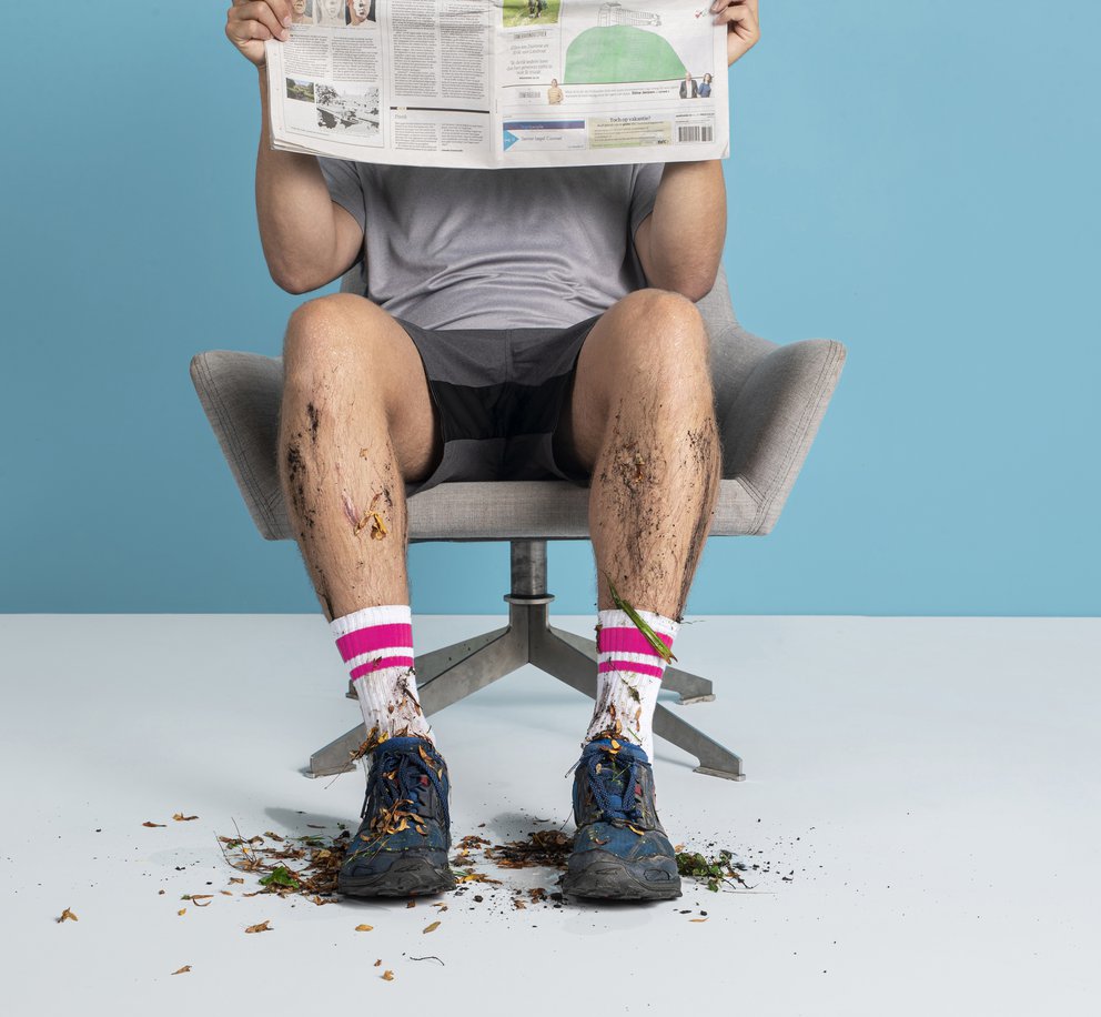 Een man die met hele vuile sportschoenen op een witte vloer zit